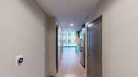 Located on the 9th floor at 511 Fayetteville Street in the heart of downtown Raleigh, NC, this one-bedroom, one-bathroom unit offers a modern urban living experience. The open layout connects the living area to a well-appointed kitchen featuring dark wood cabinetry, stainless steel appliances including a dishwasher and microwave, and a clean countertop workspace — all visible through a wide pass-through opening that enhances the sense of openness. Light wood flooring runs throughout, complementing the crisp white walls and creating a bright, cohesive aesthetic. The living area is bathed in natural light courtesy of dramatic floor-to-ceiling windows that frame sweeping views of the downtown Raleigh skyline and surrounding cityscape. The bedroom also benefits from expansive glass curtain-wall windows, filling the room with light and offering continued urban views. The bathroom is finished with contemporary fixtures, including a dark wood vanity with a white countertop, a large mirror with overhead lighting, and a glass-enclosed walk-in shower clad in neutral large-format tile with brushed nickel hardware. A hallway connects the spaces efficiently, completing this well-designed urban residence ideal for those seeking a stylish foothold in downtown Raleigh.