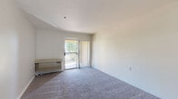 Located in Glendale, Arizona, this one-bedroom, one-bathroom unit offers a well-organized single-floor layout designed for comfortable everyday living. The living area is finished with plush wall-to-wall carpeting and neutral-toned walls that create a bright, open atmosphere. A sliding glass door leads to a private balcony, allowing natural light to fill the space while offering pleasant views of the surrounding greenery. A wall-mounted HVAC unit provides climate control directly in the living area. The kitchen is efficiently arranged in an L-shaped configuration, featuring warm wood-toned cabinetry, light countertops, wood-look vinyl flooring, and a full suite of white appliances including an electric range, dishwasher, and refrigerator — providing ample functionality within a compact footprint. The bedroom is a comfortable size, carpeted throughout, and includes a sliding closet with wood-panel doors for storage. The bathroom is well-appointed with a single-sink vanity with matching wood cabinetry, a walk-in shower equipped with grab bars and a handheld showerhead, and durable wood-look flooring. A standout feature is the in-unit stacked washer and dryer, conveniently housed within a closet adjacent to the bathroom, offering added practicality to this thoughtfully designed Glendale residence.