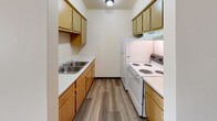 This well-appointed one-bedroom, one-bathroom unit in Oshkosh, Wisconsin offers a practical and comfortable single-floor layout. The living area features durable luxury vinyl plank flooring in a warm gray tone, neutral white walls, and a window with vertical blinds that allows natural light to fill the space. A wall-unit air conditioner and baseboard heating provide year-round climate control. The living area also includes a large sliding-door closet near the entry, offering generous storage. The galley-style kitchen is efficiently designed with light oak cabinetry, white laminate countertops, a stainless steel sink, and white appliances including a coil-burner electric range and full-size refrigerator — all set atop matching LVP flooring. The bedroom is carpeted for comfort and features a window with an exterior view, baseboard heating, and a clean, open layout suitable for various furniture arrangements. The full bathroom includes a single-sink vanity with oak cabinetry, a large wall mirror with overhead lighting, and a tub/shower combination with a white surround, all finished with LVP flooring. The overall aesthetic is clean, neutral, and move-in ready, providing a functional living space in a residential Oshkosh neighborhood.
