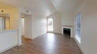 This single-story, two-bedroom, one-bathroom residence at 1540 Chennault is designed with a clean, neutral aesthetic throughout. The living room serves as the centerpiece of the home, featuring soaring vaulted ceilings that create an open, airy atmosphere. A wood-burning fireplace with a white mantel anchors one wall, while an arched window and additional large windows fitted with blinds allow generous natural light to fill the space. Dark hardwood-style flooring runs throughout the main living areas, adding warmth and contrast to the crisp white walls.

The kitchen is positioned adjacent to the living area and includes a peninsula counter with marble-look surfaces, a herringbone tile backsplash, light gray cabinetry, and black appliances including a range, microwave, and refrigerator. A front entry features a paneled door with sidelights, continuing the bright, welcoming feel.

Both bedrooms are carpeted, each equipped with a ceiling fan and windows offering outdoor views. A sliding glass door in one bedroom provides access to an exterior area. The shared bathroom is finished with large-format gray tile surrounding a soaking tub and shower combination, complemented by modern chrome fixtures and hardwood-style flooring.