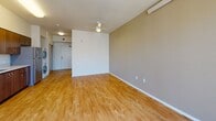 This single-floor unit offers a well-organized layout that efficiently combines living and functional spaces. The kitchen is equipped with stainless steel appliances, including an electric range and full-size refrigerator, complemented by rich warm-toned wood cabinetry extending from floor to ceiling. Light-colored countertops provide ample workspace, and an under-cabinet range hood adds practicality. A stacked washer and dryer unit is conveniently integrated into the kitchen area.

The open living space adjoins the kitchen and is finished with light hardwood flooring throughout, creating a cohesive and airy feel. Two large windows allow natural light to fill the room and offer views of the surrounding urban streetscape. Track lighting on the ceiling provides additional illumination. A ceiling fan in the bedroom area enhances comfort, while the same hardwood flooring continues seamlessly through the space.

The bathroom features a wooden vanity with a single sink, a large mirror with overhead lighting, and multiple towel bars mounted on the walls. The flooring transitions to neutral-toned tile, and the layout is designed with accessibility in mind, offering ample open space throughout.
