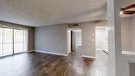 This single-floor unit presents a clean, neutral aesthetic throughout, with warm gray walls, crisp white trim, and textured ceilings that carry consistently across each room. The open living area is anchored by dark wood-style plank flooring and features a ceiling fan and a sliding glass door fitted with vertical blinds, allowing natural light to filter in while providing access to the outdoors.

The galley-style kitchen is efficiently laid out with white cabinetry, light countertops, a stainless steel refrigerator, and black appliances including a range and dishwasher. Wood-look tile flooring completes the kitchen's clean, functional design.

The bedrooms are finished with plush carpeting and feature sliding closets with built-in hanging rods. A window in one bedroom provides natural light and an outdoor view. The bathrooms include a white vanity with a mirror and lighted fixture, wood-look tile flooring, and a full tub-shower combination with a curtain rod. The layout, as seen in the floorplan, offers a logical flow between the living, kitchen, bedroom, and bathroom areas, creating a well-organized and cohesive living space.
