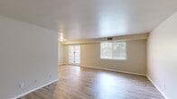 This single-story space is thoughtfully laid out across a comfortable footprint, with light wood-look flooring running consistently throughout, lending the interiors a clean, cohesive aesthetic. The living area is generously proportioned and benefits from an abundance of natural light, courtesy of a large picture window and a set of French doors that open to the outdoors, offering views of surrounding greenery. Neutral, warm-toned walls complement the pale flooring and contribute to a bright, airy atmosphere throughout.

The kitchen is efficiently arranged and features light wood cabinetry with ample upper and lower storage, dark speckled countertops, a stainless steel sink, and a white gas range with an overhead ventilation hood. The space is compact yet practical, providing all essential cooking amenities.

The bedrooms are well-sized, each featuring the same consistent flooring and neutral wall tones. Closet storage is present in each room, with one bedroom offering a walk-in closet and another equipped with bifold-door reach-in closet. Natural light enters through windows fitted with blinds. The bathroom includes a tub and shower combination with white tile surround, maintaining the unit's clean, understated finish throughout.