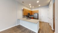 Located at 1001 W Rosedale St in Fort Worth, TX, this one-bedroom, one-bathroom unit offers a well-designed single-floor layout with a cohesive modern aesthetic. Wood-style plank flooring runs consistently throughout the space, anchoring the clean, neutral color palette of soft whites and warm grays.

The kitchen serves as a central highlight, featuring warm-toned wood cabinetry that extends floor to ceiling, a stone tile backsplash, granite-look countertops, and a full suite of stainless steel appliances including a refrigerator, electric range, and microwave. A peninsula with an integrated sink provides additional prep space and doubles as a casual dining area, illuminated by pendant lighting overhead alongside recessed ceiling lights.

The bedroom is a comfortable, well-proportioned room with two windows that invite natural light and feature blinds for privacy. It connects directly to a dedicated walk-in closet equipped with multiple shelving tiers and hanging rods, offering organized storage.

The bathroom is finished with a granite-top vanity with warm wood cabinetry, a full tub-shower combination with tile surround, and wood-style flooring consistent with the rest of the unit. The overall ambiance is clean, functional, and contemporary.