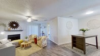 This thoughtfully designed single-floor residence offers a comfortable and functional layout across six distinct spaces, including a living room, bedroom, kitchen, closet, bathroom, and hallway. The living room serves as the heart of the home, showcasing hardwood-style flooring, a textured ceiling, a ceiling fan, and a fireplace with a classic mantel. Large vertical blinds allow for adjustable natural light, and the open feel of the space makes it ideal for both relaxing and entertaining. The kitchen features white cabinetry, light stone-finish countertops, a double stainless steel sink, and a window that brings in additional natural light. The bedroom is a generously sized retreat with its own ceiling fan, two windows, and a sliding glass door that connects to the outdoors, providing excellent ventilation and natural brightness. It also includes direct access to a dedicated walk-in closet lined with built-in shelving and hanging rods on both sides, offering ample storage. The bathroom is finished with a white vanity, stone-finish countertop, and a wide mirror with an integrated medicine cabinet. Consistent hardwood-style flooring flows throughout, tying the entire space together with a clean, cohesive aesthetic.