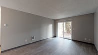 Located at 609 NE 178th Ave in Gresham, Oregon, this single-floor unit offers a straightforward, functional layout across several distinct spaces. The living area is finished with wood-style plank flooring in a cool gray tone and neutral gray walls beneath a textured ceiling. A sliding glass door fills the room with natural light and provides direct views of surrounding greenery, creating a connection to the outdoors. A wall-mounted heating unit adds a practical touch to the space.

The galley-style kitchen is efficiently organized with white cabinetry lining both walls, stainless steel sink, laminate countertops, and white appliances including a coil-top range and refrigerator. A window above the sink draws in additional natural light, brightening the workspace.

The bedroom features wall-to-wall carpet, dual windows fitted with vertical blinds for privacy and light control, and a baseboard heater. An adjacent room with wood-style flooring includes a closet and opens toward the windowed area, offering flexible use as a secondary bedroom or den.

The bathroom is cleanly appointed with a single-basin vanity, speckled countertop, framed mirror, and a full tub-shower combination with white surrounds and chrome fixtures. Throughout the unit, the consistent neutral palette and durable flooring contribute to a clean, move-in-ready environment.