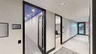 Located at 715 Park Ave in East Orange, NJ, this thoughtfully designed amenity floor offers a well-rounded collection of spaces spanning a generous single level. The layout is accessed through a sleek hallway finished with large-format tile flooring, clean white walls, and black-framed glass doors that lend a contemporary, polished aesthetic throughout.

The standout living room functions as a private home theater, featuring rows of black leather recliner chairs arranged on a light hardwood floor. Linear LED lighting runs along the ceiling perimeter, complemented by a built-in projector and wall-mounted speakers, creating an immersive cinematic atmosphere with a refined, modern finish.

The exercise room is a vibrant, energizing space defined by bold orange accent walls and durable rubberized flooring. It is fully equipped with cardio machines including treadmills, ellipticals, and stationary bikes, as well as free weights, a weight rack, and strength training equipment. Large mirrors, flat-screen TVs, and flush panel lighting make this a high-functioning fitness environment.

A compact workstation area features individual desk partitions beneath a striking cobalt blue ceiling, providing focused work zones with marble-finish tile flooring. Recessed lighting keeps the space bright and functional. A bathroom completes the floor, ensuring all essential conveniences are on hand.
