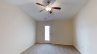 This single-story residence offers a practical and well-organized layout designed for comfortable everyday living. The open living area is finished with neutral-toned carpet and anchored by a ceiling fan with a light fixture, creating a bright and airy atmosphere. A door with a glass panel brings in natural light and provides access to the exterior. The living space flows seamlessly into the kitchen, which is visible through a pass-through opening with a granite-look countertop overhang — ideal for casual dining or entertaining. The galley-style kitchen is equipped with rich dark wood cabinetry, light stone-finish countertops, and a full suite of black appliances including a refrigerator, electric range, microwave, and dishwasher, all set on tile flooring. The bedrooms are carpeted and include ceiling fans, with the primary bedroom offering direct access to an en-suite bathroom. The bathrooms feature dark wood vanities with light countertops, tile flooring, and a tub-shower combination. A dedicated laundry room provides washer and dryer hookups along with wire shelving for added storage. Additional bedrooms are well-sized with natural window light and neutral finishes throughout.