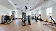 Located at 40 Mt. Eve Road in Eagle, Colorado, this fitness center offers a well-appointed, single-floor workout facility designed to accommodate a comprehensive range of exercise routines. The space features a clean, modern aesthetic with crisp white walls, a tray ceiling with a large industrial-style ceiling fan, and durable speckled flooring suited for high-traffic athletic use. Natural light floods the room through numerous windows along multiple walls, providing bright, open-air ambiance while offering views of the surrounding Colorado landscape. A wall-mounted flat-screen television is positioned for easy viewing during cardio sessions. The facility is equipped with a robust selection of Matrix-brand strength training machines, including cable and weight stack systems, as well as free-weight benches and functional training attachments. The cardio section features multiple treadmills, elliptical trainers, and a stationary recumbent bike, all arranged to maximize usability within the space. A water station and waste receptacles are conveniently available near the entrance. Track lighting and recessed fixtures supplement the natural light, ensuring consistent visibility throughout the facility. The entrance features a glass-paneled door, contributing to the open and welcoming character of this well-maintained fitness center.