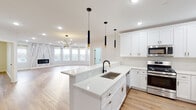This thoughtfully designed single-floor residence showcases a bright, open-concept layout with premium finishes at every turn. The heart of the home is a stunning kitchen featuring crisp white shaker cabinetry adorned with sleek black and gold hardware, a large center island with a quartz waterfall countertop and undermount sink, a stylish matte black faucet, and a full marble-look backsplash. Stainless steel appliances, including a gas range, over-the-range microwave, and French door refrigerator, complete this chef-inspired space. Pendant lighting with gold accents hangs above the island, complementing the sputnik chandelier that anchors the adjacent living area. The spacious living room is a standout, featuring a dramatic marble-surround linear fireplace flanked by a curved bay of windows that floods the space with natural light. Warm-toned luxury vinyl plank flooring flows seamlessly throughout. The primary bathroom offers a navy vanity with gold fixtures, a backlit LED mirror, and marble-look tile flooring, with a walk-in closet conveniently adjacent. A secondary bathroom echoes the clean aesthetic with white marble tile and a bright window. Additional bedrooms provide versatile, well-lit spaces with ample storage.