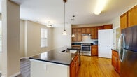 Located at 8117 Evening Star Dr in Pasadena, Maryland, this well-appointed one-bedroom, one-bathroom residence offers a thoughtfully designed single-floor layout with generous living space. The open-concept kitchen and living area serves as the heart of the home, featuring warm honey-toned hardwood flooring, rich wood cabinetry, dark granite countertops, stainless steel appliances including a gas range and refrigerator, and a central kitchen island with pendant lighting overhead. The seamless flow between the kitchen and living area creates an inviting, functional space ideal for everyday living. The spacious primary bedroom is carpeted for comfort and bathed in natural light through a bank of large windows, with a ceiling fan adding to the airy feel. The bedroom includes dual closets — one walk-in and one reach-in — providing ample storage. Additional windows throughout offer pleasant neighborhood views. The bathroom features a full tub-shower combination with white and brown accent tiling, along with accessibility grab bars and a wood-vanity cabinet. A dedicated utility room rounds out the layout. Warm neutral tones are carried throughout, creating a cohesive and comfortable ambiance across the entire residence.
