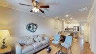 This two-story residence offers two bedrooms and two and a half bathrooms within a efficiently arranged floor plan. The main living area features an open-concept layout that seamlessly connects the living room, dining area, and kitchen, creating a cohesive and functional space ideal for both everyday living and entertaining.

The living room is appointed with crown molding, recessed lighting, and a ceiling fan, contributing to a comfortable and well-lit atmosphere. Light-toned walls and wood-look flooring run throughout the main level, enhancing the sense of openness. A dedicated dining area bridges the living space and kitchen, accommodating a full dining table with ample room for guests.

The kitchen is outfitted with white cabinetry, stainless steel appliances, and a kitchen island with seating, offering both prep space and casual dining options. The overall design maintains a clean, coastal-inspired aesthetic with neutral tones accented by soft blues and natural textures. With two full bedrooms, a convenient half bath on the main level, and a two-story layout, this residence provides practical separation between living and sleeping areas.