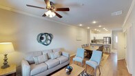 This two-story residence offers two bedrooms and two and a half bathrooms within a efficiently arranged floor plan. The main living area features an open-concept layout that seamlessly connects the living room, dining area, and kitchen, creating a cohesive and functional space ideal for both everyday living and entertaining.

The living room is appointed with crown molding, recessed lighting, and a ceiling fan, contributing to a comfortable and well-lit atmosphere. Light-toned walls and wood-look flooring run throughout the main level, enhancing the sense of openness. A dedicated dining area bridges the living space and kitchen, accommodating a full dining table with ample room for guests.

The kitchen is outfitted with white cabinetry, stainless steel appliances, and a kitchen island with seating, offering both prep space and casual dining options. The overall design maintains a clean, coastal-inspired aesthetic with neutral tones accented by soft blues and natural textures. With two full bedrooms, a convenient half bath on the main level, and a two-story layout, this residence provides practical separation between living and sleeping areas.