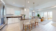 Located in Bradenton, FL, this well-appointed single-story home offers 3 bedrooms and 2 bathrooms across a thoughtfully designed open floor plan. Light wood-look tile flooring flows through the main living areas, creating a cohesive, airy aesthetic complemented by crisp white walls and abundant natural light.

The welcoming entrance leads down a bright hallway into the heart of the home. The combined living, dining, and kitchen area serves as the social hub, where the living room features a striking tray ceiling and expansive sliding glass doors that open directly to the patio — ideal for indoor-outdoor living. The kitchen is outfitted with white shaker-style cabinetry, dark countertops, stainless steel appliances, and a peninsula with bar seating.

Both bathrooms are finished with light tile flooring, white vanities, dark countertops, and clean subway-tiled showers. The primary bedroom is generously sized, accompanied by a walk-in closet with built-in shelving. A secondary hallway leads to the additional bedrooms, which feature plush carpeting and share access to a well-appointed full bath.

The paved patio provides a comfortable outdoor retreat. A dedicated laundry room with full-size washer and dryer hookups and an attached garage with an automatic opener round out this functional and stylish Florida home.