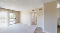This 2-bedroom, 1-bathroom residence in Escondido, California is thoughtfully laid out across a single floor, offering a functional and comfortable living arrangement. The living room is a generously sized, open area featuring plush carpeting, neutral beige walls, a textured ceiling, and vertical blinds framing a sliding glass door that brings in natural light and provides outdoor access. The kitchen is well-appointed with white cabinetry, granite-style countertops, wood-look vinyl flooring, and white appliances including a range and built-in microwave, making efficient use of the available space. Both bedrooms are carpeted and bathed in natural light through windows dressed with vertical blinds. The primary bedroom offers a comfortable footprint along with a sliding-door closet for ample storage. The second bedroom is similarly sized with a window overlooking the outdoors. The shared bathroom features wood-look vinyl flooring, a white vanity with granite-style countertops, and a full tub-shower combination with a window above for ventilation. A hallway connects the rooms, contributing to a cohesive and easy-to-navigate floor plan. The consistent warm, neutral palette throughout the home creates a clean, move-in-ready ambiance.