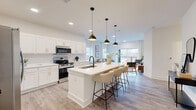 Located at 175 Black St in Rock Hill, SC, this well-appointed 2-bedroom, 2-bathroom residence offers a thoughtfully designed single-floor layout with a generous overall footprint. The open-concept living area seamlessly connects the kitchen, dining space, and living room, creating an inviting and functional hub for daily life. The kitchen is a standout feature, showcasing white shaker cabinetry with gold hardware, a white quartz waterfall island with bar seating, a subway tile backsplash, stainless steel appliances, and striking matte black and brass pendant lighting. Light wood-tone flooring flows throughout the main living areas, enhancing the bright, airy atmosphere. The living room opens to a private balcony through large sliding glass doors dressed with floor-to-ceiling drapes, allowing abundant natural light. The primary bedroom is a comfortable retreat with plush carpeting, and its en-suite bathroom features a double vanity with gold hardware, large-format marble-look tile, and a glass-enclosed walk-in shower. The second bathroom offers a full soaking tub with marble-style tile surround. Additional highlights include a dedicated office, in-unit laundry, a pantry, a utility room, and four closets—including a walk-in with wire shelving—providing excellent storage throughout.