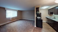 This single-floor unit offers a practical and comfortable layout designed for everyday living. The galley-style kitchen is efficiently organized, featuring dark espresso cabinetry on both sides, light granite-style countertops, a stainless steel sink, and black appliances including a refrigerator and range. Wood-look flooring runs through the kitchen, providing a clean, durable surface underfoot.

The open living and dining area transitions seamlessly from the kitchen, highlighted by warm, neutral-toned walls and plush carpeting that adds comfort and coziness. A large window with vertical blinds allows natural light to fill the space, while a wall-mounted air conditioning unit ensures year-round climate control. A pendant light fixture adds a subtle decorative touch to the dining area.

The bedroom is generously sized with soft carpeting, neutral walls, and a wide window that frames outdoor views and invites natural light. A baseboard heater and wall AC unit offer individualized climate management.

The bathroom is outfitted with a full tub and shower combination featuring a white surround, clean chrome fixtures, and a classic, functional design. Throughout the unit, white baseboards and neutral wall tones create a cohesive, understated aesthetic that is move-in ready and easy to personalize.