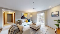 This single-floor residence offers a thoughtfully arranged layout that balances open communal spaces with comfortable private retreats. The living room serves as the heart of the home, featuring neutral gray walls, soft carpeting, and large French doors that invite abundant natural light and provide direct access to an outdoor area. A bold abstract artwork anchors the main wall, complementing the contemporary furnishings and layered area rug beneath.

The living space flows seamlessly into a dedicated dining area, defined by wood-look flooring that transitions from the carpeted lounge zone. A compact, well-equipped galley kitchen runs parallel to both walls, featuring warm honey-toned cabinetry, white countertops, recessed lighting, and full appliances including a dishwasher, range, and refrigerator.

A hallway connects the main living areas to two bedrooms, each carpeted and bathed in natural light from generously sized windows. The primary bedroom includes both a walk-in closet and an en-suite bathroom, while a second full bathroom with a tub-shower combination serves the remainder of the residence. Both bathrooms feature wood-look flooring and warm wood vanity cabinetry, maintaining a consistent aesthetic throughout the home.