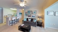 This single-story residence offers a well-organized layout with multiple functional spaces finished in warm neutral tones throughout. The living room features plush carpeting, crown molding, a ceiling fan with light fixture, and large windows that allow ample natural light. An adjacent dining area showcases crown molding details and a decorative chair rail, creating a defined yet open space. The kitchen is designed in a galley style with white cabinetry, light countertops, white appliances, and tile flooring, with direct access to an in-unit laundry area. Multiple bedrooms are present, each carpeted and equipped with ceiling fans. One bedroom includes a walk-in closet, while others feature standard closet storage. The bedrooms receive natural light through windows dressed with curtain panels. Two bathrooms mirror each other in design, each offering a shower-tub combination, vanity with storage cabinetry, light countertops, and tile flooring. The consistent use of neutral wall colors, carpet in living and sleeping areas, and tile in wet areas creates a cohesive and practical aesthetic throughout the residence.