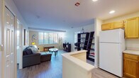 This single-floor unit is designed with an open, functional layout that connects key living areas seamlessly. The kitchen features warm honey-toned wood cabinetry, white appliances including a refrigerator, electric range, and microwave, along with recessed lighting and a peninsula that opens toward the main living space. Light wood-style flooring runs consistently throughout, enhancing the sense of continuity and space.

The living area is generously sized, anchored by large windows with vertical blinds that allow natural light to fill the room. A ladder-style open shelving unit serves as a stylish divider between the living and dining zones. A dedicated office or flex room sits adjacent to the main living space, featuring its own window and ample room for a full desk setup.

Two bedrooms offer comfortable proportions, each with windows providing natural light and sufficient space for standard furnishings. The full bathroom includes a tub-shower combination equipped with accessibility grab bars, a wood-toned vanity with a countertop sink, and wood-style tile flooring. Throughout the unit, warm neutral wall tones and consistent flooring create a cohesive, calm ambiance.