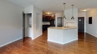 Located at 5001 Olentangy River Rd in Columbus, Ohio, this single-floor residence offers a thoughtfully designed layout with a cohesive blend of comfort and functionality. The open-concept living and kitchen area serves as the heart of the home, anchored by gleaming hardwood-style flooring that extends throughout the main living spaces. Large windows allow natural light to pour in, enhancing the bright and airy atmosphere of the living room.

The kitchen is well-equipped and visually striking, featuring rich dark espresso cabinetry that extends to the ceiling for ample storage, tile backsplash accents, and light stone countertops. A peninsula with pendant lighting and a built-in sink provides additional workspace and a casual dining option. Black appliances, including a side-by-side refrigerator, electric range with over-the-range microwave, and dishwasher, complete the kitchen. A dedicated in-unit laundry area is conveniently accessible nearby.

The bedroom offers plush carpeting, neutral walls, and a generous walk-in closet with built-in shelving. A second carpeted bedroom provides natural light through a large window. The bathroom features hardwood-style flooring consistent with the main living areas. Throughout the space, dark-paneled interior doors provide a polished contrast to the neutral color palette.