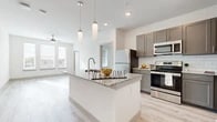 This well-appointed single-floor residence offers a bright, contemporary design with a cohesive neutral palette throughout. The open-concept kitchen serves as the heart of the home, anchored by a spacious granite-topped island with an undermount sink and stylish pendant lighting overhead. Gray shaker-style cabinetry, a classic white subway tile backsplash, and a full suite of stainless steel appliances — including a range, microwave, and refrigerator — complete the kitchen's modern aesthetic. Light wood-look flooring flows seamlessly through the kitchen and main living areas, creating a clean, unified look.

The living area extends naturally from the kitchen, bathed in natural light from large windows fitted with horizontal blinds. A ceiling fan adds both function and style to the space. The bedrooms continue the bright, airy feel, featuring plush carpeting, ceiling fans, and multiple windows that invite natural light and outdoor views. Each bedroom offers generous proportions suited for comfortable living.

The bathroom is finished with the same attention to detail, showcasing a dual-sink granite vanity with gray cabinetry, a large mirror, and light wood-look flooring that mirrors the rest of the home. The overall ambiance is clean, modern, and move-in ready.