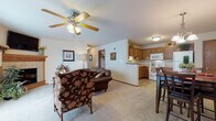 Located at W6866 Blue Heron Blvd in Fond du Lac, Wisconsin, this single-floor unit offers a practical and comfortable layout designed for easy living. The open-concept living and dining area is highlighted by plush carpeting, neutral walls, and a ceiling fan that enhances airflow and light. A tiled fireplace with a classic wood mantel serves as the focal point of the living room, complemented by a wall-mounted TV above. The kitchen is efficiently designed with warm oak cabinetry, light countertops, a double stainless steel sink, and white appliances including a range and built-in microwave. Tile flooring in the kitchen adds durability and easy maintenance. A dedicated dining area with tile flooring transitions naturally from the kitchen, providing a comfortable space for meals. The bedroom features soft carpeting, a window with blinds for natural light control, and a closet with sliding wood doors. Two bathrooms serve the unit — one with oak vanity cabinetry and a white countertop, and another with tile flooring and a lighted vanity mirror. Throughout the space, warm wood trim, oak doors, and cohesive neutral tones create an inviting and well-maintained atmosphere suited for comfortable, everyday living.