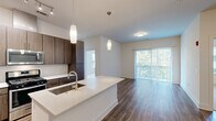 This thoughtfully designed 2-bedroom, 2-bathroom residence offers a seamless open-concept layout that maximizes both functionality and comfort. The kitchen serves as the centerpiece of the living area, featuring rich dark wood cabinetry, a white quartz waterfall island with an undermount sink, a white subway tile backsplash, and a full suite of stainless steel appliances including a gas range, microwave, and French door refrigerator. Elegant pendant lighting illuminates the island, complementing the track lighting overhead. Hardwood-style flooring flows throughout the main living areas, leading to a spacious living room with direct access to an outdoor area through sliding glass doors fitted with vertical blinds. The bedrooms are carpeted for comfort, with the primary bedroom offering multiple windows with outdoor tree views and a ceiling fan. Each bedroom is supported by its own closet with wire shelving systems. Both bathrooms are finished with quartz countertops, wood-toned vanities, large mirrors, and tile flooring. One bathroom features a tub-shower combination with floor-to-ceiling tile surround, while the other offers a dual-sink vanity with direct access to the primary bedroom. The overall aesthetic is clean, modern, and move-in ready.