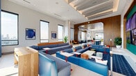 Located in the heart of Midtown Atlanta, this generously sized amenity lounge spans nearly 3,000 square feet across a single floor, offering a thoughtfully designed social hub with distinct zones for relaxation, entertainment, and recreation. The space is anchored by a dramatic large-format media wall framed in rich teal, set against an eye-catching textured mosaic feature wall. Expansive sectional seating in shades of navy and sky blue fills the main lounge area, arranged around low tables to encourage conversation and gathering. Soaring ceilings with layered acoustic baffles and abundant recessed lighting create a bright, airy atmosphere throughout. A separate lounge area features a striking blue-painted ceiling inset, oversized pendant lights, plush mint-green velvet sofas, and colorful geometric area rugs, giving it a distinct residential warmth. Floor-to-ceiling windows frame sweeping views of the Atlanta skyline, flooding the space with natural light. A game area includes a foosball table and direct access to an outdoor terrace adorned with vibrant murals. Additional nooks offer high-top seating alongside green upholstered banquettes, a billiards area, and warm wood accents throughout, making this a versatile and visually dynamic amenity space.