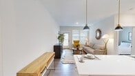 This two-story residence offers a well-organized layout across two floors, with the more spacious main level housing the primary living areas and the upper level accommodating additional private spaces. The main floor features an open-concept design where the kitchen flows naturally into the dining and living areas. The kitchen is outfitted with white flat-front cabinetry, a subway tile backsplash, stainless steel appliances including a refrigerator with ice maker, electric range, and microwave, and a peninsula with seating for casual dining. Dual pendant lights with brass hardware add a modern accent. The living area extends toward a glass-panel door that invites natural light and provides outdoor access. Hardwood-style flooring runs throughout the main level, complementing the neutral, light-toned walls. Both bedrooms feature plush carpeting, ceiling fans, and windows with exterior views. The bathrooms are well-appointed, with one showcasing marble-style tile in the walk-in shower and a clean white vanity. Three closets provide ample storage, and a dedicated laundry area with a top-loading washer adds convenience. The overall aesthetic is clean, contemporary, and functional.