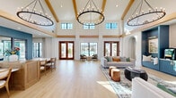 Located at 1010 Rosefinch Landing in Hoschton, GA, this single-story community clubhouse is a masterfully designed gathering space that blends elegance with comfort. The grand main hall commands immediate attention with its soaring double-height ceilings, exposed wood beam accents, and dramatic wrought-iron chandelier. Light hardwood flooring in a herringbone pattern flows throughout, while an abundance of floor-to-ceiling windows and French doors with rich wood framing flood the interior with natural light and provide sweeping views of the outdoor pool area. Graceful arched doorways connect the various lounge and social zones, creating a seamless flow between spaces. A sophisticated sitting lounge features a striking stone fireplace as its focal point, complemented by curated leather seating. A boutique library room, finished in deep blue with built-in shelving, offers an intimate retreat. An art-forward lounge showcases a curated gallery wall against a sage-green accent wall, while a stylish nook with upholstered banquette seating and brass accent lighting adds a refined, intimate touch. The dining area features a botanical mural accent wall, marble-top tables, and bar-height seating. Throughout, the design balances modern sophistication with warm, inviting details.