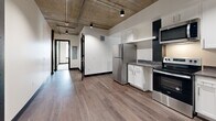 Located at 708 22nd Street in Greeley, Colorado, this two-bedroom, two-bathroom unit delivers a striking industrial-modern aesthetic across a well-proportioned single-floor layout. The design is defined by signature exposed concrete ceilings with visible ductwork and track lighting, bold dark door and window trim, and crisp white walls — a cohesive palette that lends the space a contemporary urban character.

The kitchen is a functional highlight, featuring stainless steel appliances including a refrigerator, range, microwave, and dishwasher, complemented by white shaker cabinets, dark stone-style countertops, and warm wood-tone hardwood flooring that extends through the main living areas.

Both bedrooms are carpeted for comfort, each with a window fitted with blinds and a wall-mounted PTAC unit for individualized climate control. The generously sized primary bedroom includes a dedicated closet. The industrial ceiling aesthetic carries throughout both rooms, maintaining design continuity.

The two bathrooms are clean and modern in finish. One features a full soaking tub with white subway tile surround, a floating vanity with a matte black faucet, and wood-tone flooring. The second is a compact, efficient full bath with a similarly minimalist aesthetic.

Two additional closets provide practical storage throughout the unit, rounding out this well-designed Greeley residence.