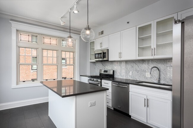 York House designer kitchen with gas stove, quartz countertops, stainless steel appliances, marble kitchen backsplash, and slate tile floor. - York House