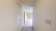 Located at 5100 Highbridge St in Fayetteville, NY, this single-floor, one-bedroom, one-bathroom unit offers a well-organized layout across a comfortable footprint. The interior is finished with neutral cream-toned walls throughout, creating a bright and cohesive aesthetic.

The living area is generously proportioned, featuring soft wall-to-wall carpeting and multiple HVAC vents for year-round comfort. A second living space provides additional flexibility for dining or a home office setup. Tile flooring transitions the hallways, connecting rooms with a clean, practical finish.

The kitchen is a functional highlight, showcasing rich dark-wood cabinetry with raised panel detailing, light granite countertops, a stainless steel sink, and a dishwasher. A coffered ceiling detail adds visual interest overhead, while a sliding glass door leads to an outdoor area, allowing natural light to flow in.

The primary bedroom is a comfortable retreat, carpeted and bathed in natural light from a window overlooking lush, wooded surroundings — a serene and private outdoor view. The full bathroom includes a full-size soaking tub with a shower, chrome fixtures, and a grab bar, offering both comfort and accessibility.

Three hallways efficiently connect the various spaces, and ample closet storage is accessible throughout the unit.