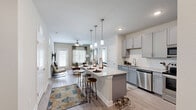 This thoughtfully designed single-story model home in Lady Lake, Florida offers a functional and stylish layout across two bedrooms and two full bathrooms. The open-concept living area is bright and welcoming, with light wood-style flooring, large windows that invite natural light, a ceiling fan, and a glass door providing outdoor access. The kitchen is a standout, outfitted with granite countertops, grey shaker-style cabinetry, a white subway tile backsplash, and a full suite of stainless steel appliances including a range, microwave, dishwasher, and refrigerator. The primary bedroom is generously sized, featuring soft carpet, a ceiling fan, and a distinctive whitewashed brick accent wall. Its en-suite bathroom includes a dual-sink vanity with granite countertops, grey cabinetry, wood-style flooring, and a glass-enclosed walk-in shower. A dedicated walk-in closet with wire shelving completes the primary suite. The second bedroom is equally comfortable, with carpet flooring, a ceiling fan, and ample natural light. The second bathroom features a granite vanity and a tiled tub-shower combination. Two closets provide practical storage throughout the home.