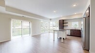 This single-floor unit is designed with a modern, open-concept layout that seamlessly connects the living and kitchen areas. The living space features light hardwood-style flooring, neutral-toned walls, and a sliding glass door that opens to a private balcony, allowing ample natural light to fill the room. Architectural beam detailing adds subtle visual interest to the ceiling.

The kitchen is well-equipped with rich dark espresso cabinetry, granite countertops, a white subway tile backsplash, and stainless steel appliances including a refrigerator, range, microwave, and dishwasher. A central island with a white base and granite top provides additional workspace and storage, complemented by open floating shelves.

The bedrooms feature plush carpet flooring, neutral walls, and windows with outdoor views. The primary bedroom includes a ceiling fan and access to a generously sized walk-in closet outfitted with multi-tiered wire shelving systems for organized storage.

The bathroom is finished with dark cabinetry, granite countertops, an undermount sink, brushed nickel hardware, a large framed mirror, and a tall storage cabinet. Hardwood-style flooring carries throughout, maintaining a cohesive, contemporary aesthetic across the entire unit.