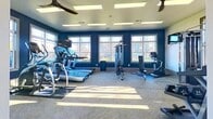 This 470 square foot fitness center in Glenmoore, PA, offers a comprehensive workout experience within a single-floor layout. The space is characterized by its abundance of natural light, streaming through large windows that line the walls, providing an open and energizing atmosphere. The interior design features a striking contrast of crisp white walls accented by vibrant blue sections, creating a dynamic and motivating environment.

The gym is equipped with a wide array of exercise machines, including treadmills, ellipticals, stationary bikes, and weight training equipment. A dedicated area for free weights and strength training is evident, complete with benches and rack systems. Cardiovascular equipment is strategically placed near the windows, allowing users to enjoy outdoor views while exercising.

The facility's layout is well-organized, with clear zones for different types of workouts. The flooring appears to be a durable, low-maintenance material suitable for high-traffic gym use. Ceiling-mounted fluorescent lighting supplements the natural light, ensuring even illumination throughout the space.

Additional amenities include wall-mounted TVs for entertainment, ceiling fans for air circulation, and convenient storage solutions for small equipment like exercise balls and resistance bands. The entrance area features glass doors, contributing to the overall sense of openness and accessibility.

This thoughtfully designed fitness center provides a welcoming and functional space for various workout routines, catering to diverse fitness needs within its compact yet efficient 470 square foot area.