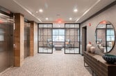Located at 968 Bonnel Ct in Union, New Jersey, this polished single-floor commercial space offers a thoughtfully designed professional environment with a contemporary aesthetic. The layout is anchored by striking floor-to-ceiling black-framed glass partition walls, which allow natural light to flow between areas while maintaining a sense of privacy and openness simultaneously.

A dedicated private office features a warm wood-toned desk, wall-mounted display screen with pendant lighting overhead, and direct access to natural light through exterior windows — creating a productive yet inviting workspace. Adjacent to this area, a comfortable lounge space is furnished with a pair of upholstered wingback chairs accented with colorful throw pillows, arranged around a low coffee table. The lounge is flanked by large windows dressed with solar roller shades that filter daylight while framing views of the surrounding streetscape.

Throughout the space, textured geometric-patterned wall coverings in deep charcoal tones lend a sophisticated, design-forward quality. Recessed ceiling lighting provides consistent illumination, complemented by the abundant natural light. Neutral patterned carpeting grounds the space and ties the design elements together cohesively. Framed artwork adorns the walls, adding a curated, professional character to the overall environment.