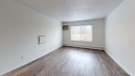 This single-floor unit at 345 Firwood Dr in Dayton, Ohio, offers a straightforward, functional layout spread across several distinct rooms. Wood-style plank flooring runs consistently throughout the space, providing a cohesive look and easy maintenance. White walls and neutral tones give each room a clean, bright appearance.

The spacious living area features a textured ceiling, a wall-mounted air conditioning unit, and a baseboard heating system, ensuring year-round climate control. A large window allows natural light to filter in, offering views of the surrounding outdoor greenery. An additional access panel is mounted on the wall, contributing to the room's practical design.

The bedroom areas are generously sized, each equipped with baseboard heating and windows fitted with blinds for privacy and light control. One bedroom includes a ceiling fan with a light fixture, a sliding closet, and a built-in countertop surface, while a dedicated walk-in closet with dual shelving rods provides ample storage.

The kitchen is efficiently organized in a galley-style configuration, featuring white cabinetry, granite-look countertops, and included appliances such as a refrigerator and a range. Wood-style flooring continues seamlessly into this space. The unit's single-level design ensures easy accessibility throughout.