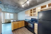 Located at 2360 Lawrence St in Denver's vibrant Cole/RiNo neighborhood, this efficiently designed studio offers a single-floor layout that incorporates a living room, kitchen, and full bathroom. The space is defined by its striking exposed concrete ceiling, which lends an industrial urban character throughout. Track lighting illuminates the kitchen and entry areas, adding both functionality and a modern aesthetic touch.

The kitchen is well-appointed with light wood cabinetry — including open upper shelving for easy access — dark countertops, and a full suite of black appliances including a range, dishwasher, and refrigerator. Wood-look flooring runs seamlessly through the kitchen and into the living area, creating visual continuity across the space.

The living area benefits from large, multi-pane windows that invite natural light and offer views of the surrounding Denver cityscape. A wall-mounted HVAC unit provides climate control. The room's neutral walls and light flooring keep the space feeling open and airy.

The bathroom features a clean, white tub-shower combination with a curtain rod, complemented by wood-look flooring consistent with the rest of the unit. The entryway provides a clean transition point into the space. Compact yet thoughtfully organized, this studio is well-suited for urban living in one of Denver's most dynamic neighborhoods.