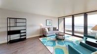 This well-designed single-floor residence offers a thoughtfully arranged layout that balances modern style with everyday functionality. The kitchen is a standout feature, showcasing a large island with a built-in cooktop, crisp white countertops, dark cabinetry, white subway tile backsplash, stainless steel appliances, and a striking ceiling-mounted range hood that serves as a focal point of the space. Wood-style flooring flows through the main living areas, creating a cohesive and contemporary feel throughout.

The living area is bright and inviting, with large sliding glass doors that open to a private balcony offering sweeping city and skyline views. Natural light fills the room, complementing the neutral tones and modern furnishings. An adjacent dining area, also with balcony access and city views, provides an ideal space for entertaining.

The bedrooms are carpeted and tranquil, each featuring a closet and neutral wall tones that foster a restful atmosphere. The bathrooms are clean and functional, equipped with dark wall-mounted cabinetry, a pedestal sink, and a glass-enclosed shower. Throughout the residence, the design maintains a consistent modern aesthetic with a neutral palette accented by contemporary fixtures and finishes.
