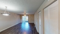 This single-floor residence offers a well-organized layout that flows naturally between its primary living spaces. The main living area features rich, dark hardwood-style flooring that extends throughout, complemented by a textured ceiling and a ceiling fan with integrated lighting. Vertical blinds frame a sliding glass door that allows natural light to fill the room, while a louvered closet provides convenient storage.

The adjoining dining area connects seamlessly to the kitchen via a pass-through window with a mirrored surround, creating an open sightline and enhancing the sense of space. The kitchen itself is equipped with dark lower cabinetry contrasted by white upper cabinets, light quartz-style countertops, a classic white subway tile backsplash, an electric range, and a sink — all beneath a textured ceiling with overhead ventilation.

The bedrooms feature plush carpeted flooring, ceiling fans, and horizontal blinds on the windows that allow for natural light control. Each room offers a calm, neutral palette with ample wall space.

The bathroom includes a clean, white walk-in shower stall, a toilet, and a vanity with a single-basin sink and a medicine cabinet mirror. Consistent neutral-toned walls and textured ceilings are found throughout the unit, lending a cohesive and practical character to the entire space.