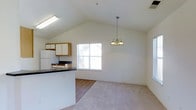 This classic two-story home offers three bedrooms and two and a half bathrooms across a well-utilized floor plan. The main living area immediately impresses with its vaulted ceilings that lend a sense of openness and volume to the space. An elegant chandelier hangs as a focal point above the living area, complementing the bright, airy atmosphere created by natural light streaming through a prominent window. The flooring transitions from hard surface in the kitchen zone to plush carpet in the living area, delineating the two spaces while maintaining a cohesive flow. The kitchen features a peninsula counter with dark countertops, white upper cabinetry, and includes standard appliances. The peninsula provides both workspace and a casual bar-style seating option. The open-concept connection between the kitchen and living area makes the main floor feel expansive and social. With 2.5 bathrooms distributed across two floors, the layout accommodates both private and guest needs efficiently. The combination of vaulted ceilings, natural light, and thoughtful spatial planning gives this home a welcoming and functional character throughout.