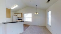 This classic two-story home offers three bedrooms and two and a half bathrooms across a well-utilized floor plan. The main living area immediately impresses with its vaulted ceilings that lend a sense of openness and volume to the space. An elegant chandelier hangs as a focal point above the living area, complementing the bright, airy atmosphere created by natural light streaming through a prominent window. The flooring transitions from hard surface in the kitchen zone to plush carpet in the living area, delineating the two spaces while maintaining a cohesive flow. The kitchen features a peninsula counter with dark countertops, white upper cabinetry, and includes standard appliances. The peninsula provides both workspace and a casual bar-style seating option. The open-concept connection between the kitchen and living area makes the main floor feel expansive and social. With 2.5 bathrooms distributed across two floors, the layout accommodates both private and guest needs efficiently. The combination of vaulted ceilings, natural light, and thoughtful spatial planning gives this home a welcoming and functional character throughout.