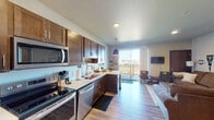 This single-floor residence offers a thoughtfully designed open-concept layout that seamlessly connects the kitchen and living area. The kitchen is well-equipped with rich dark-wood cabinetry, light countertops, and a full suite of stainless steel appliances, including a refrigerator, range, microwave, and dishwasher. A peninsula with pendant lighting serves as a natural divider between the kitchen and the adjoining living space, which benefits from abundant natural light streaming through a sliding glass door that opens to a private balcony with open outdoor views.

The living area provides a comfortable, functional space with durable hardwood-style flooring that extends throughout the main living areas. Two bedrooms offer carpeted flooring and ceiling fans, providing a cozy retreat. Each bedroom includes closet storage, and the primary bedroom features direct access to a walk-in closet. The full bathroom is finished with tile flooring, a wide vanity with a vessel-style sink, and ample counter space. A dedicated in-unit laundry closet with a stacked washer and dryer adds everyday convenience. The unit's cohesive neutral palette and modern finishes create a clean, contemporary ambiance throughout.