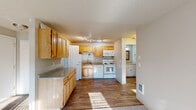 This single-floor residence offers a practical and well-organized layout designed for comfortable everyday living. The kitchen serves as a central functional hub, outfitted with warm honey-toned wood cabinetry spanning both upper and lower sections, stone-look countertops, and a full suite of white appliances including a refrigerator, electric range, built-in microwave, and dishwasher. A single-basin sink with a modern faucet is positioned beneath wall-mounted cabinetry, maximizing efficiency within the space. Rich hardwood-style flooring runs through the kitchen and connecting areas, adding warmth and durability underfoot. The living area is carpeted and bathed in natural light from a large window, creating a bright and inviting atmosphere. A separate carpeted bedroom offers a quiet retreat, also benefiting from natural light through a window with blinds. The bathroom is clean and straightforward, featuring a combination tub and shower enclosure, toilet, and a vanity with light countertops and white cabinetry, complemented by wood-look flooring. The entry area transitions smoothly into the main living space, with textured ceilings present throughout. The layout flows naturally between rooms, offering a cohesive and functional single-level living experience.