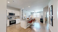 This well-appointed 2-bedroom, 2-bathroom residence offers a thoughtfully designed open-concept floor plan that seamlessly connects the kitchen, dining, and living areas. The kitchen is equipped with stainless steel appliances — including a refrigerator, range, and microwave — complemented by crisp white cabinetry, granite countertops, a tile backsplash, and a built-in breakfast bar with seating. An adjacent built-in shelving unit adds both function and character to the space. Light wood-style flooring flows continuously throughout the entire residence, enhancing the bright, airy atmosphere.

The living room features a ceiling fan and a large window that fills the space with natural light. The primary bedroom is a comfortable retreat, complete with a ceiling fan, an en-suite bathroom, and a walk-in closet outfitted with wire shelving. The en-suite bathroom features a white vanity with granite countertops and a tub/shower combination. The second bedroom is well-sized with its own access to the second full bathroom. Both bathrooms mirror the same clean, modern finishes found throughout the home. Each bedroom includes dedicated closet space, ensuring ample storage. The overall design palette of soft grays and whites lends the residence a clean, contemporary aesthetic.