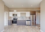 Located at 10506 121 Avenue NW in Edmonton, Alberta, this two-bedroom, one-bathroom unit offers a well-designed single-floor layout with a clean, contemporary aesthetic throughout. Light-toned luxury vinyl plank flooring runs consistently across the space, complementing warm beige walls and crisp white trim to create a bright, cohesive atmosphere.

The kitchen is a standout feature, equipped with stainless steel appliances — including a range, over-the-range microwave, dishwasher, and refrigerator — dual-tone cabinetry pairing white uppers with grey wood-grain lowers, light countertops, and a subtle subway tile backsplash. This kitchen flows naturally into a sun-filled living area with a large window and access to a private balcony overlooking the Edmonton cityscape.

The spacious primary bedroom benefits from an oversized window with panoramic city views and generous natural light, while dual closets provide ample built-in storage. The second bedroom also features light-filled windows and good closet space. The full bathroom is finished with tile surround and includes a soaker tub with overhead shower.

Baseboard heating is present throughout, and recessed lighting in the main living area adds a polished touch. The unit's elevated position offers appealing views of the surrounding Edmonton skyline.