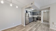 This single-floor unit offers a thoughtfully updated interior with a cohesive neutral palette and wood-look flooring throughout the main living areas. The kitchen is a standout feature, boasting grey shaker-style cabinetry, granite countertops, a classic white subway tile backsplash, and a full suite of stainless steel appliances including a refrigerator, range, microwave, and dishwasher. The kitchen opens directly to the dining and living areas, creating a connected, functional flow. The dining area is accented by a contemporary multi-pendant light fixture, adding a modern touch to the space. The open living area provides generous room for flexible furniture arrangements and is bathed in a bright, airy atmosphere thanks to neutral wall tones and consistent lighting. The bedroom features plush carpeting, a ceiling fan, and a window that allows natural light to filter in. A closet area within the bedroom also houses a convenient stacked washer and dryer unit. The bathroom is finished with matching grey cabinetry, granite countertops, an undermount sink, brushed nickel fixtures, and a round frameless mirror, maintaining the clean, modern aesthetic found throughout the rest of the unit. Textured ceilings and crisp white trim complete the well-maintained interior.