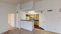 This single-floor residential unit offers a functional and comfortable layout designed for everyday living. The open-concept living area is generously proportioned, featuring soft wall-to-wall carpeting, a textured ceiling, and multiple windows that invite natural light throughout the space. A vaulted ceiling accent in the living zone adds a sense of openness and height, enhancing the overall airy feel.

The kitchen is positioned centrally and separated from the living area by a peninsula counter with a dark granite-style surface, providing both a visual divider and additional workspace. Warm oak cabinetry lines the kitchen walls from base to upper levels, complemented by white appliances including a refrigerator and an electric range with overhead ventilation. Dark hardwood-style flooring grounds the kitchen area.

Two carpeted bedrooms offer comfortable retreats, each featuring windows that bring in natural light and ceiling-mounted light fixtures. One bedroom benefits from notably elevated ceilings, creating a bright, open atmosphere.

Both bathrooms are well-appointed, each featuring a tub-shower combination with tiled surrounds, a wood-framed vanity with a dark countertop, a single undermount sink, and a lighted mirror above. Textured ceilings and hardwood-style flooring complete each bathroom's practical design.